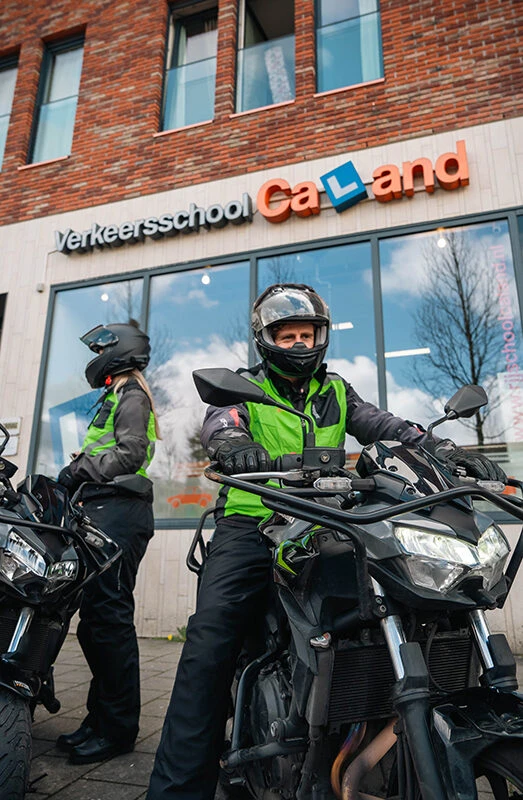 Two students from Driving School Caland are sitting on heavy motorcycles in front of the Amsterdam branch, ready for training for the motorcycle A license.