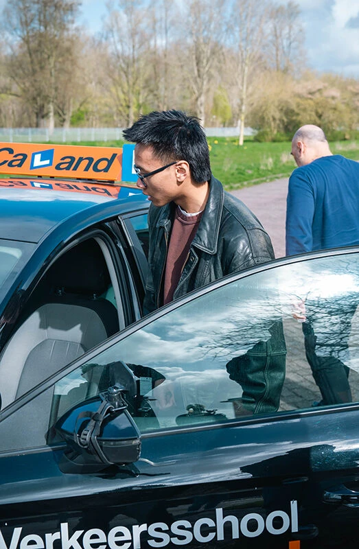 Lachende leerling stapt in bij een lesauto van Rijschool Caland voor zijn praktijkexamen in Amsterdam.