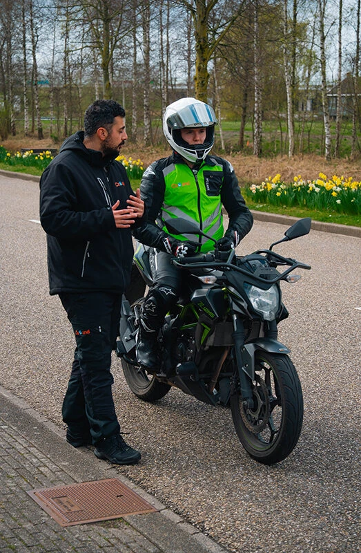 Een instructeur van Rijschool Caland geeft een leerling persoonlijke uitleg op de motor tijdens een A2 motorrijles in Amsterdam.
