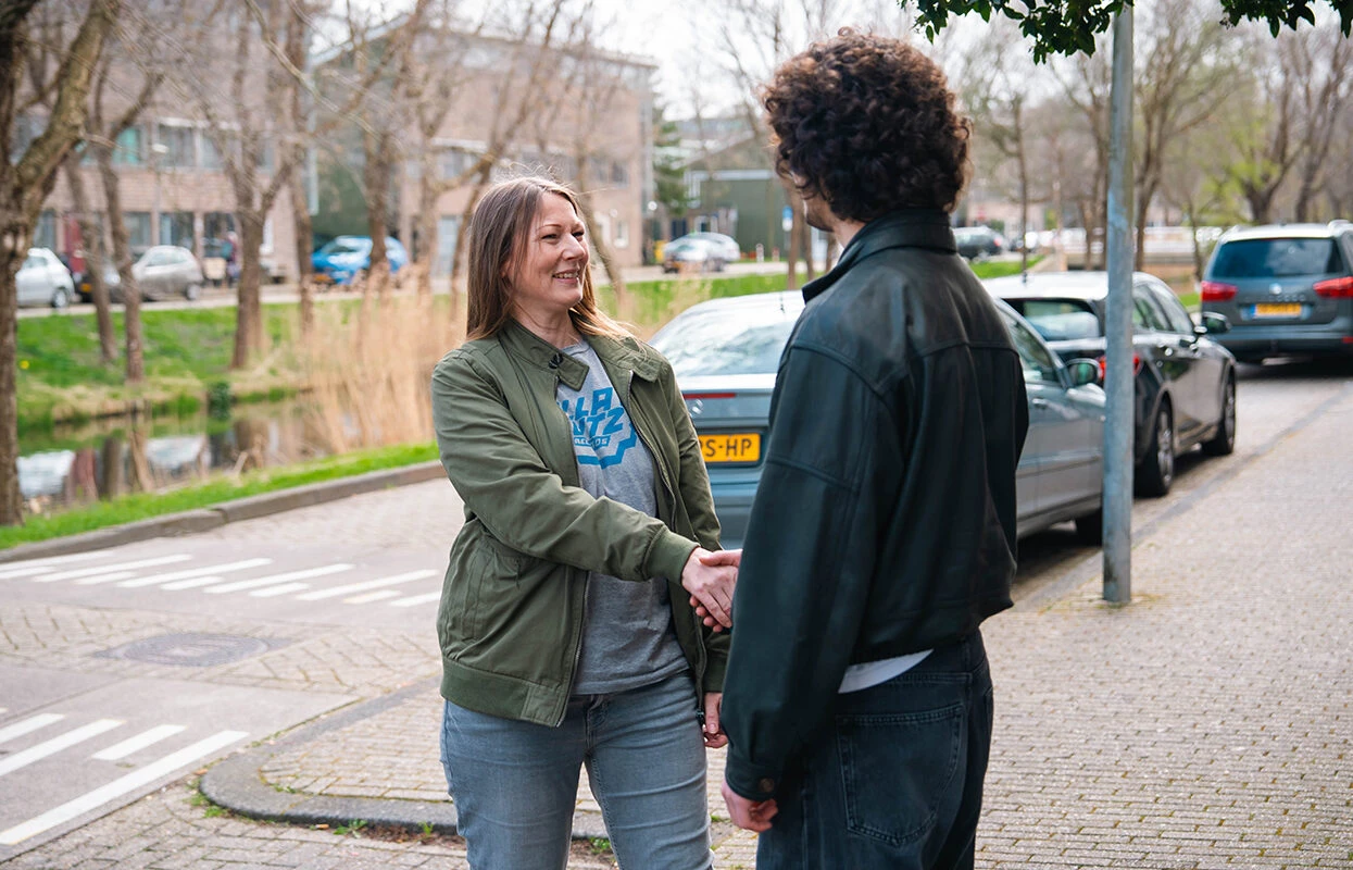 Leerling geeft een hand aan een instructeur van Rijschool Caland tijdens een kennismaking op straat in Amsterdam, voorafgaand aan een rijles.