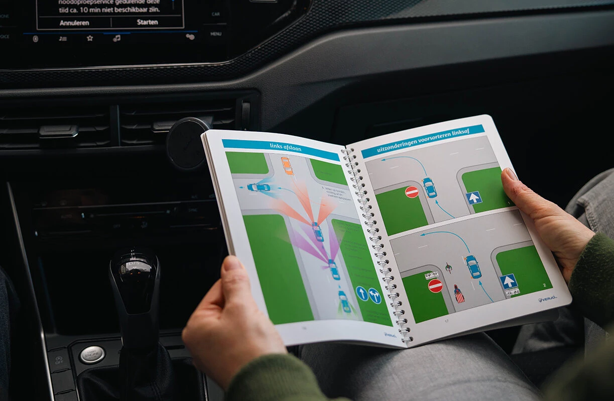 Een leerling van Rijschool Caland Amsterdam leest het theorieboek in de lesauto, met uitleg over links afslaan en voorsorteren.