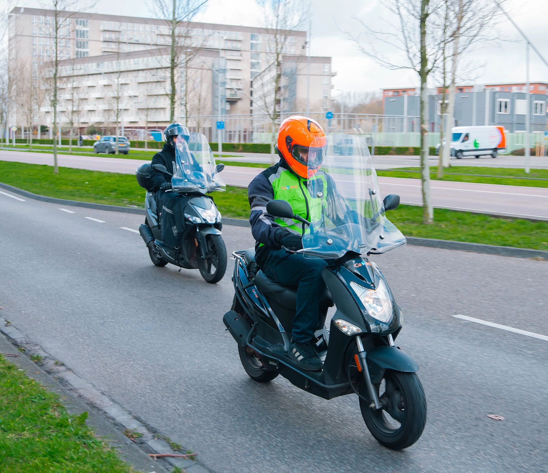 Een leerling en instructeur van Rijschool Caland rijden samen op scooters door Amsterdam tijdens een scooterles.