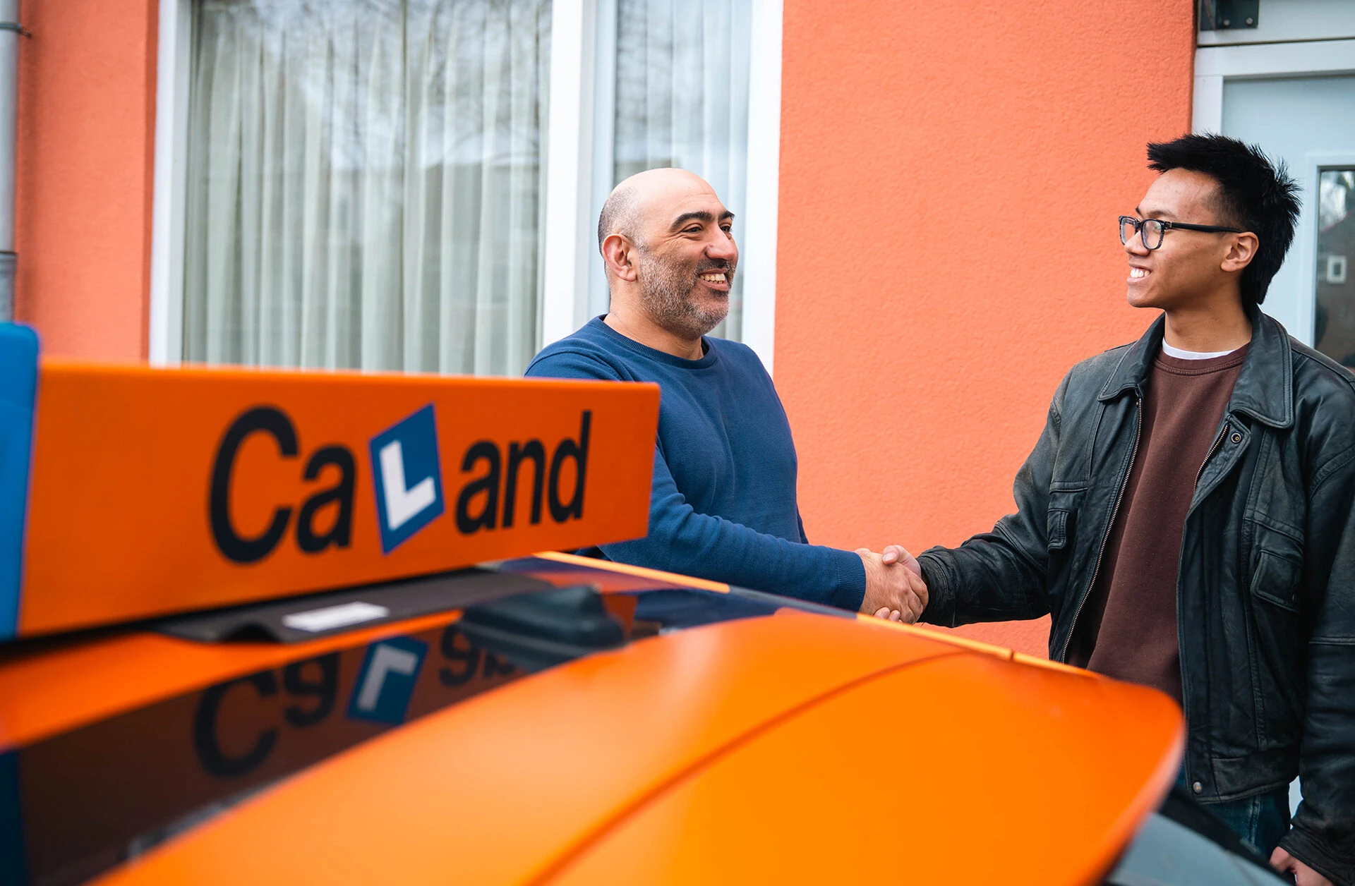 Een leerling geeft een instructeur van Verkeersschool Caland een hand bij de lesauto, als eerste stap naar een overzichtelijk rijlespakket in Amsterdam Nieuw-West.