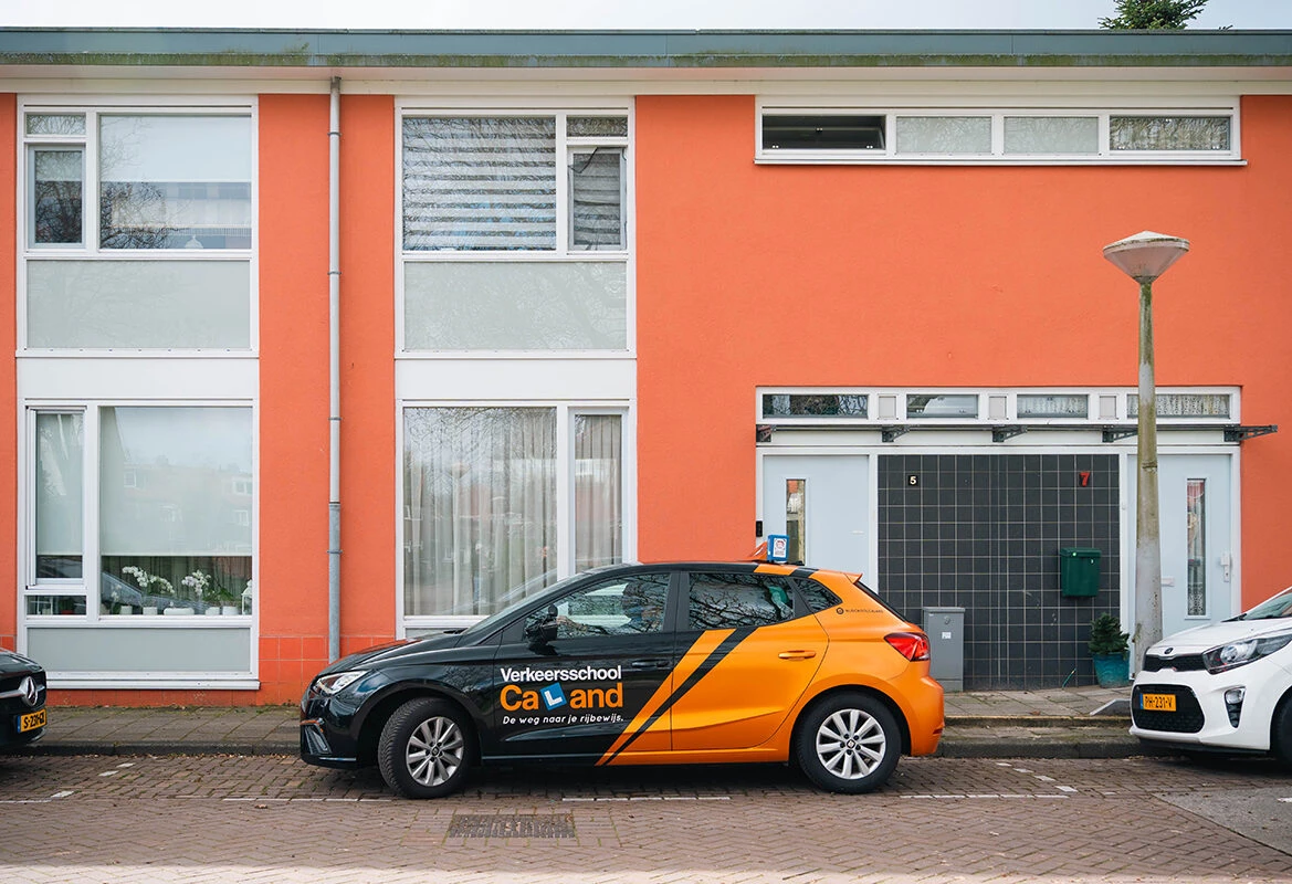 De lesauto van Rijschool Caland staat geparkeerd langs een woonstraat in Amsterdam, als onderdeel van het oefenen van bijzondere verrichtingen zoals de parkeeropdracht.