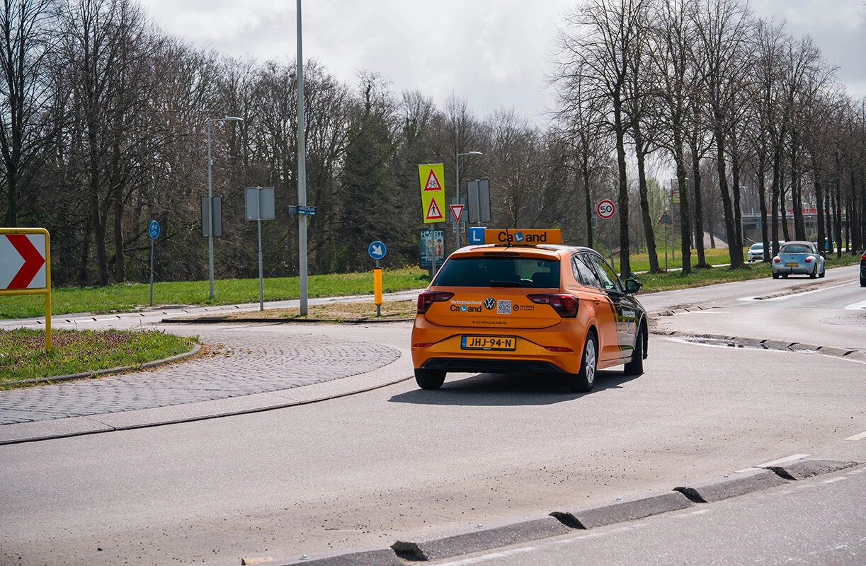 Lesauto van Rijschool Caland rijdt over een kruispunt in Amsterdam tijdens een rijles, met duidelijk zichtbare L-bord en verkeersborden langs de weg.