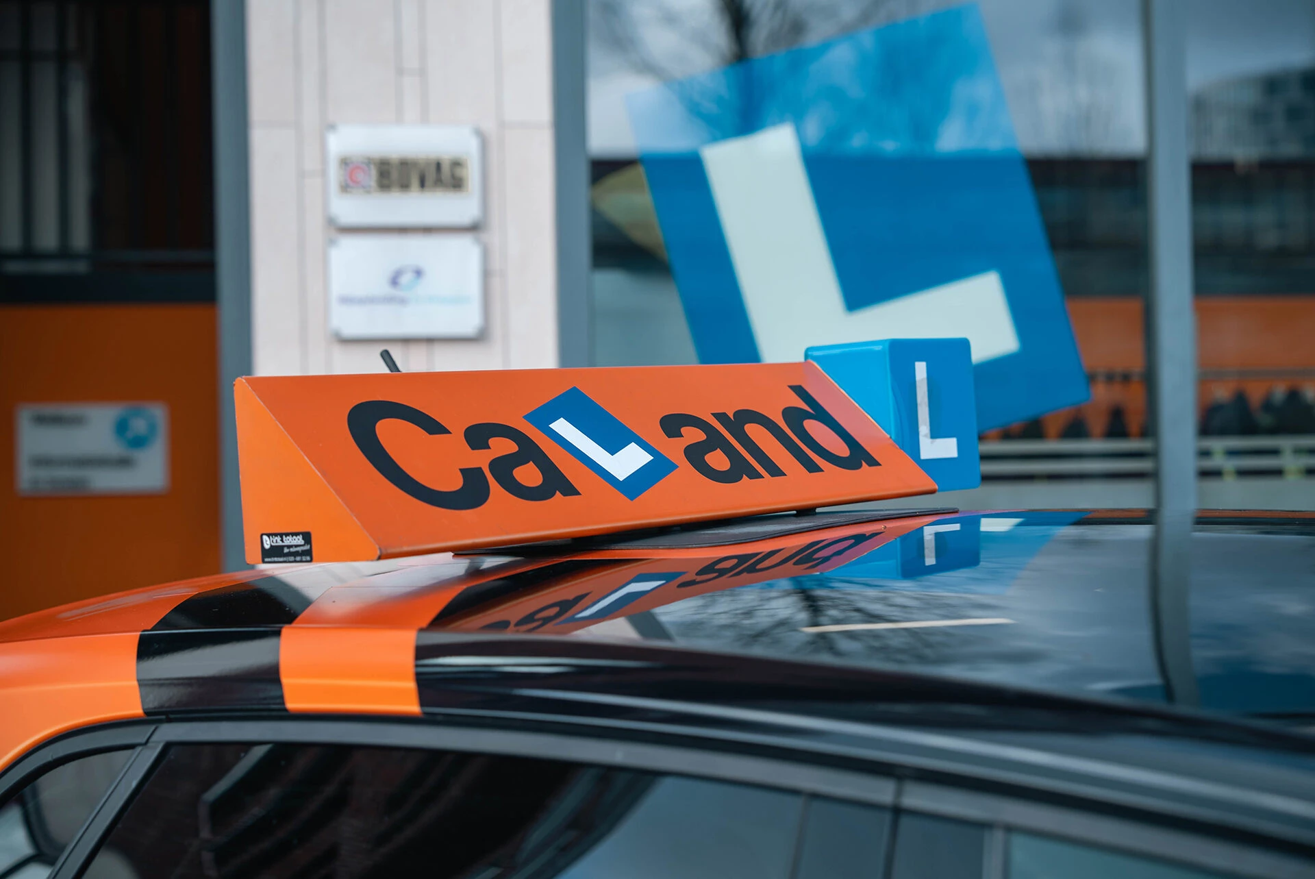 De herkenbare oranje lesauto van Verkeersschool Caland staat voor de rijschoollocatie in Amsterdam, startpunt voor een rijopleiding met duidelijke kosten en overzicht in 2026.