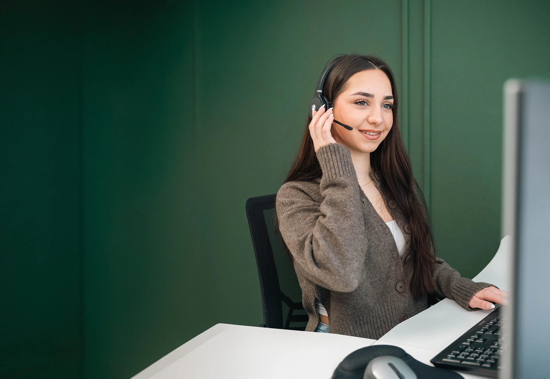 Een office manager van Verkeersschool Caland beantwoordt met een headset op vriendelijk vragen van leerlingen via telefoon en computer.