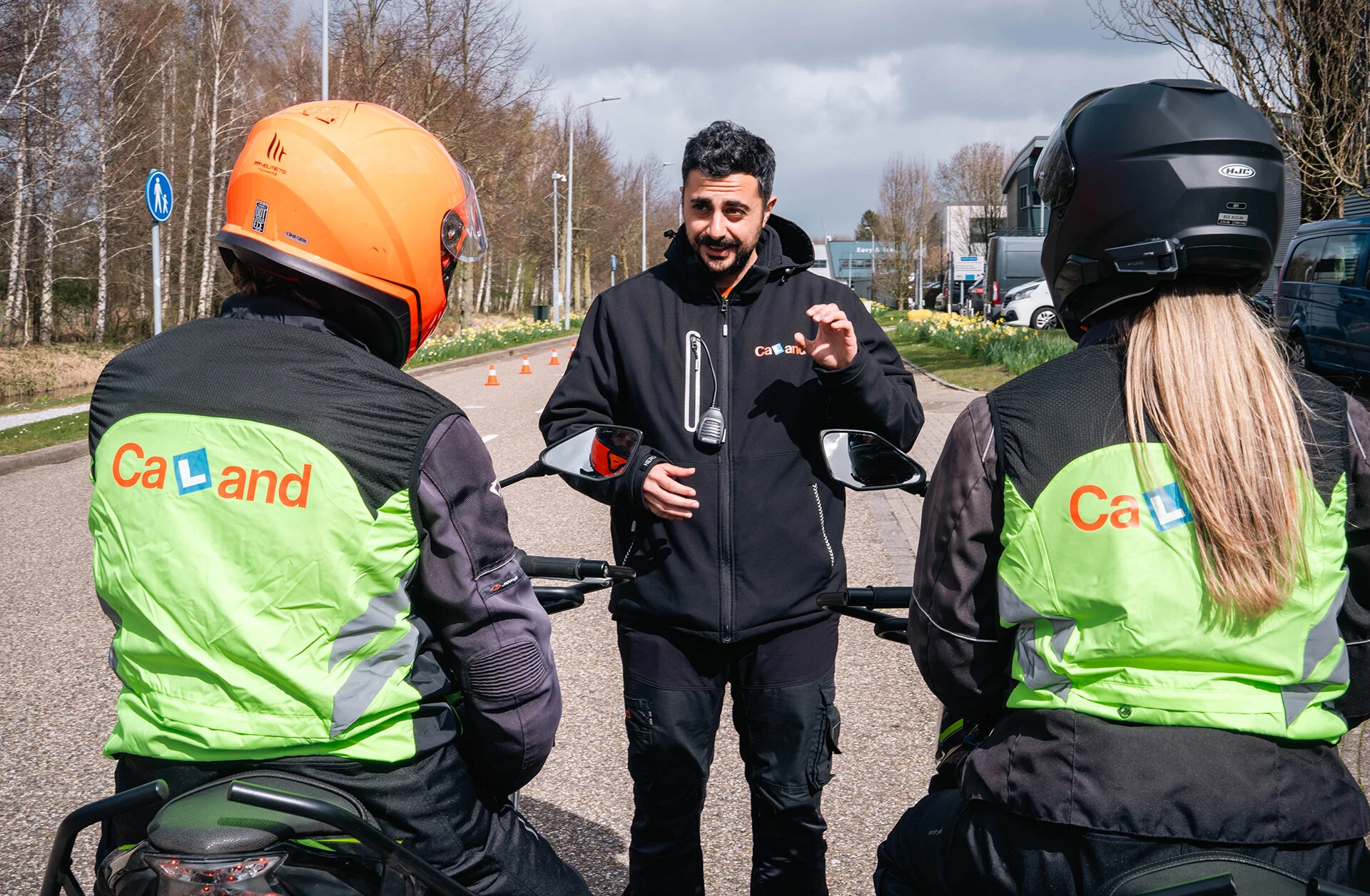Een motor-instructeur van Verkeersschool Caland geeft uitleg aan twee leerlingen op de motor tijdens een praktijkles in Amsterdam, passend bij de vacature voor motor instructeur.